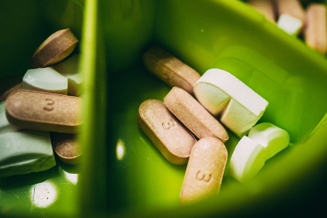 Green pill organiser showing two different types of oblong pills in white and beige colours.